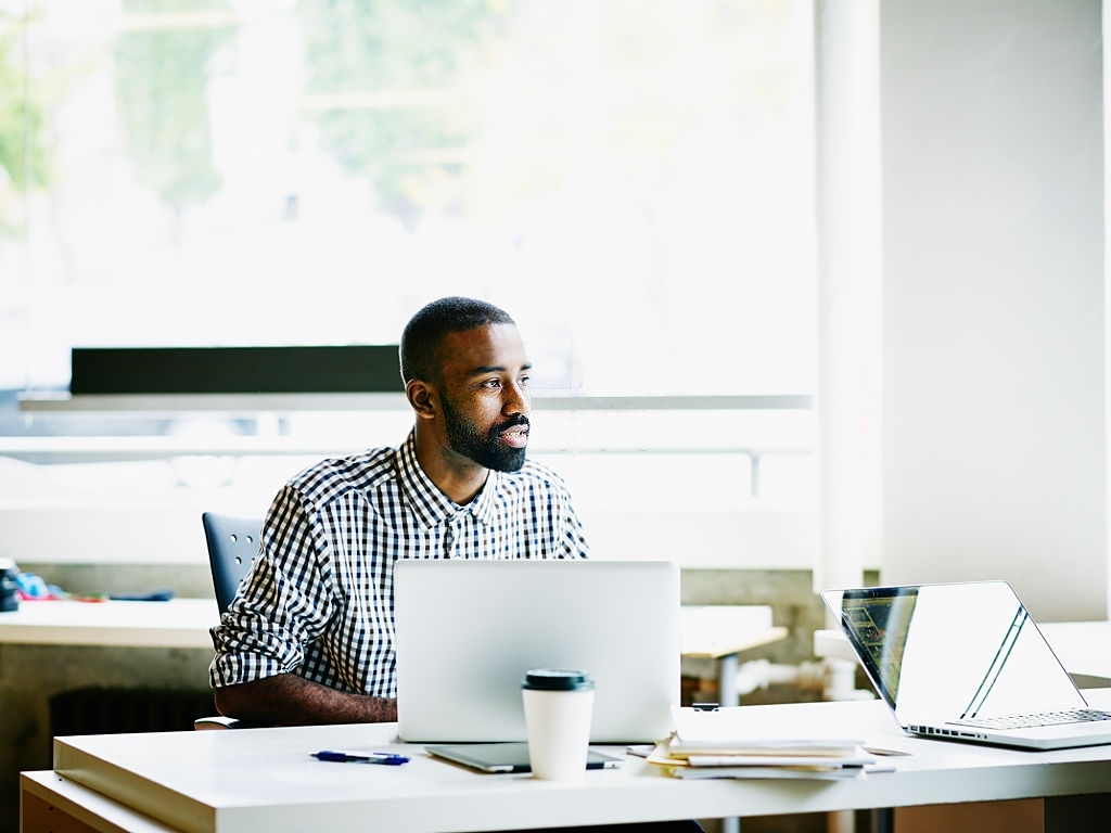 Businessman working on laptop at workstation in office looking out window